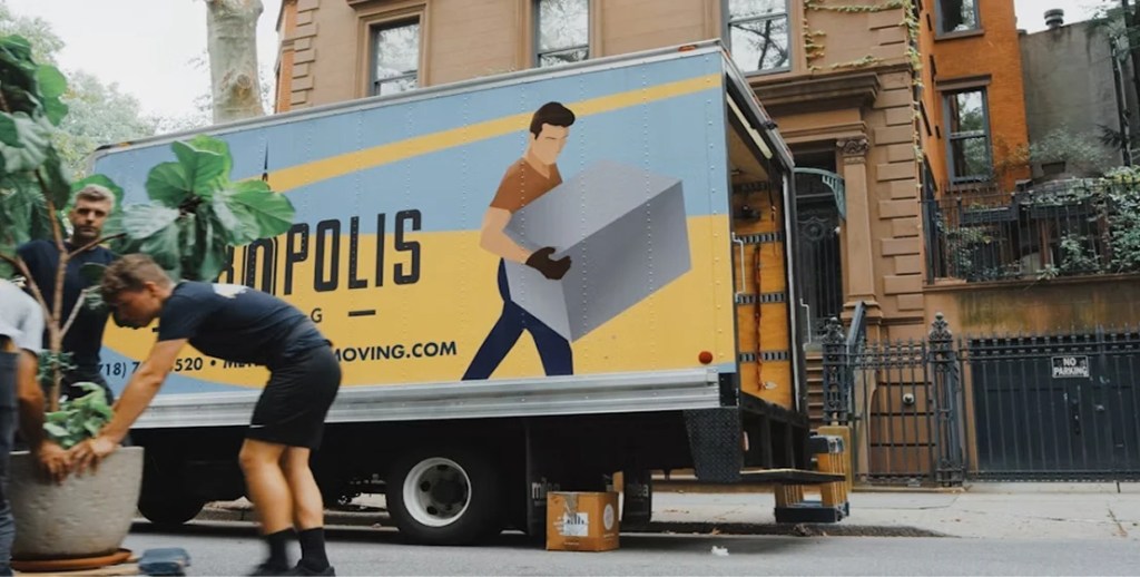 Mover carrying boxes to a moving truck parked on a city street